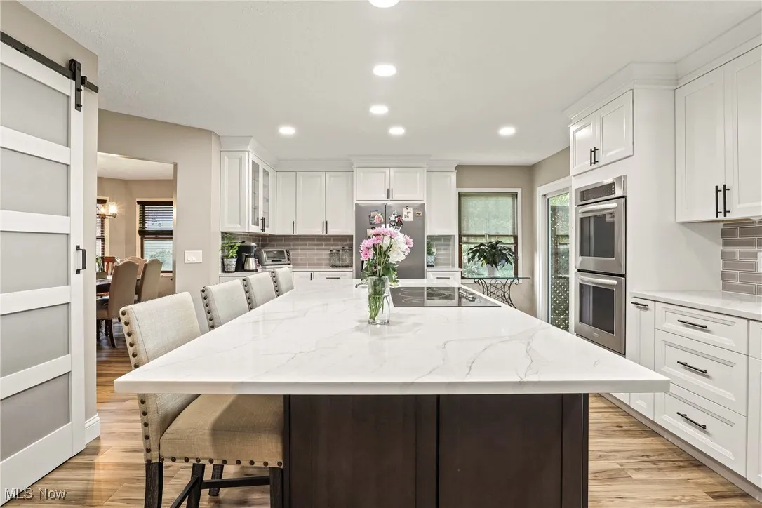 Kitchen featuring appliances with stainless steel finishes, light wood-style flooring, a kitchen bar, tasteful backsplash, and recessed lighting