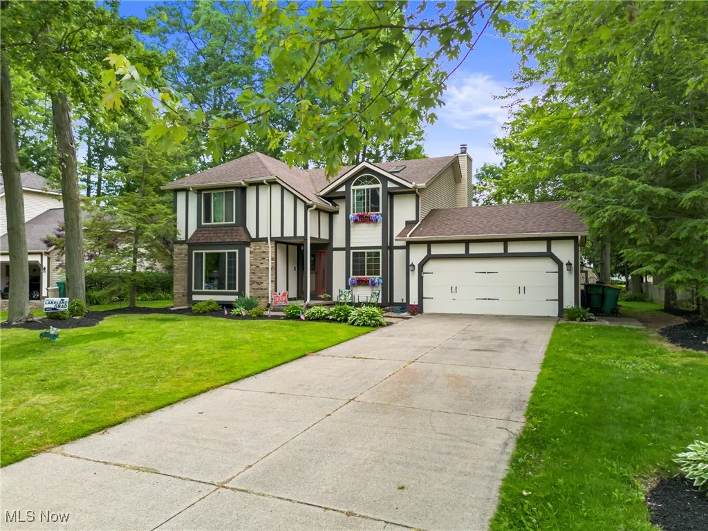 English style home featuring an attached garage, concrete driveway, a front lawn, a chimney, and brick siding