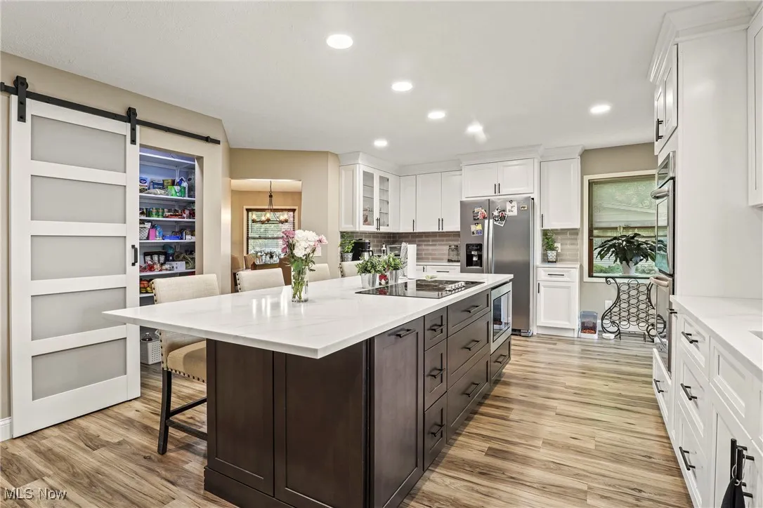 Kitchen featuring stainless steel appliances, white cabinetry, light wood-style floors, a breakfast bar area, and recessed lighting