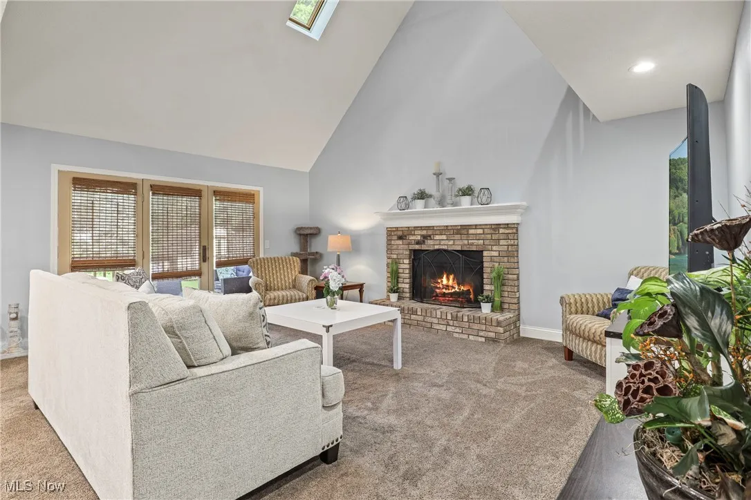Living area featuring carpet floors, a fireplace, plenty of natural light, high vaulted ceiling, and a skylight