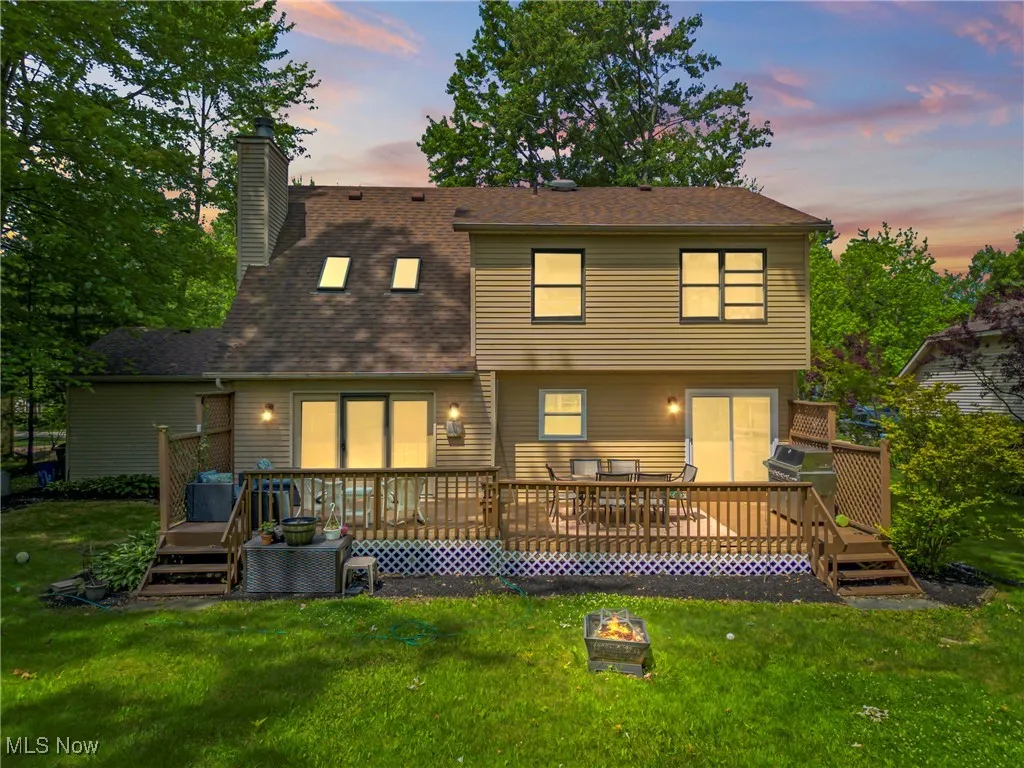 Back of property at dusk with an outdoor fire pit, a chimney, a deck, and a lawn