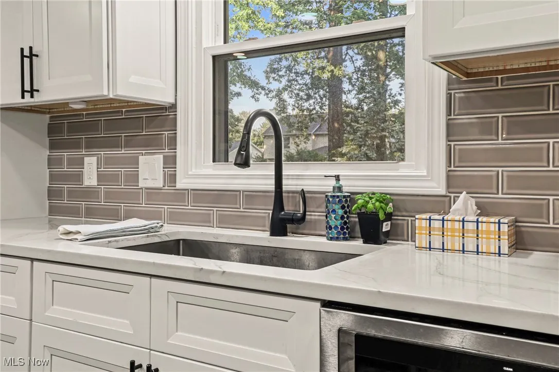 Kitchen with white cabinets, backsplash, light stone counters, and beverage cooler
