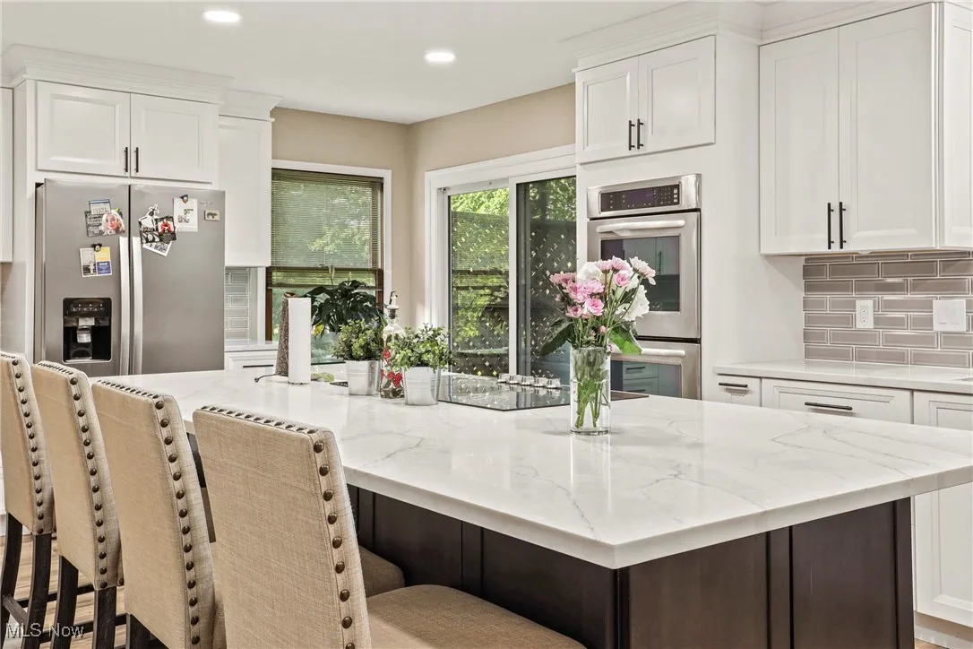 Kitchen featuring stainless steel appliances, backsplash, white cabinetry, a kitchen island, and light stone countertops