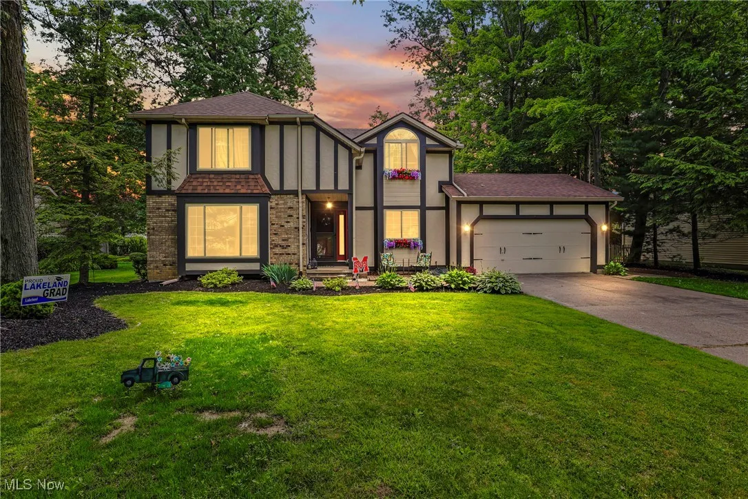 Tudor house with a garage, driveway, a lawn, and a shingled roof