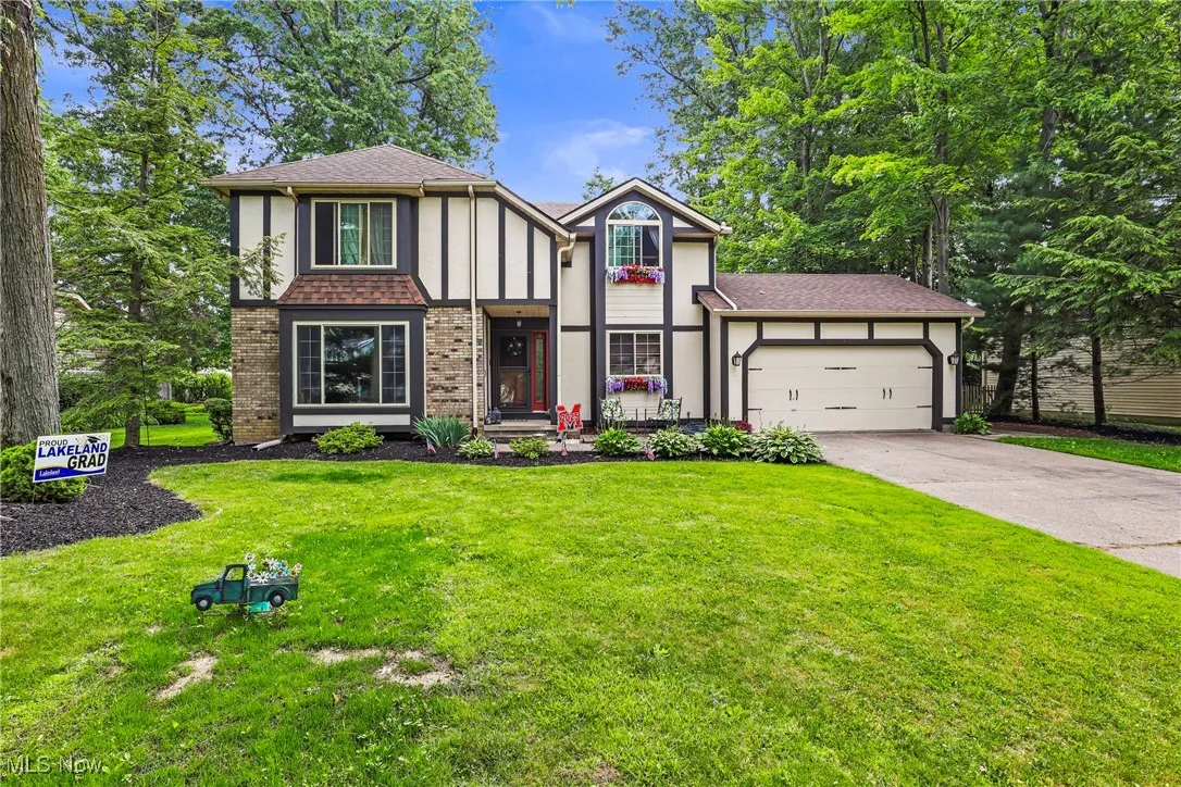 Tudor house with an attached garage, concrete driveway, a front yard, a shingled roof, and stucco siding