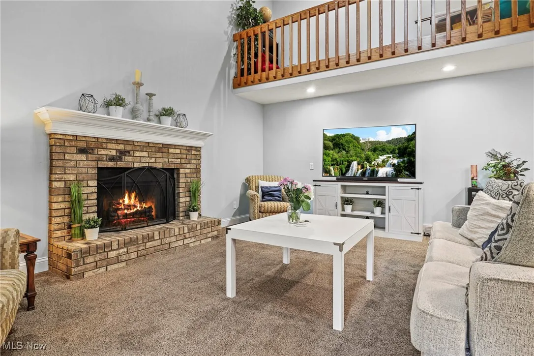 Carpeted living area featuring a brick fireplace, a towering ceiling, and recessed lighting