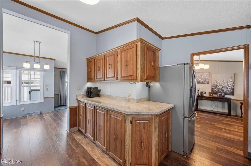 Kitchen featuring dark wood-style flooring, stainless steel refrigerator with ice dispenser, brown cabinets, and crown molding
