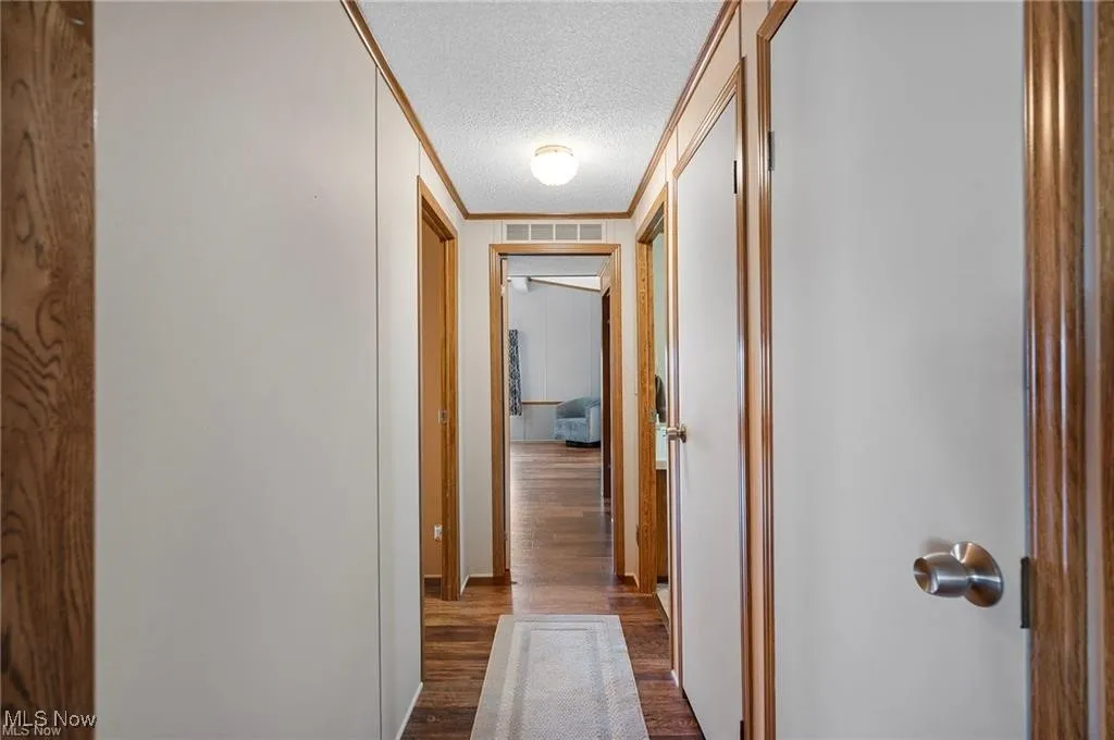 Corridor with ornamental molding, a textured ceiling, and dark wood-style flooring