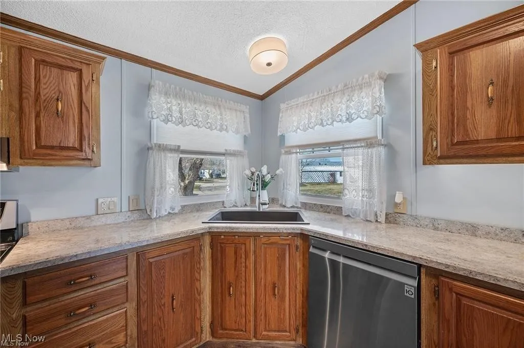 Kitchen with dishwasher, brown cabinets, ornamental molding, a textured ceiling, and lofted ceiling