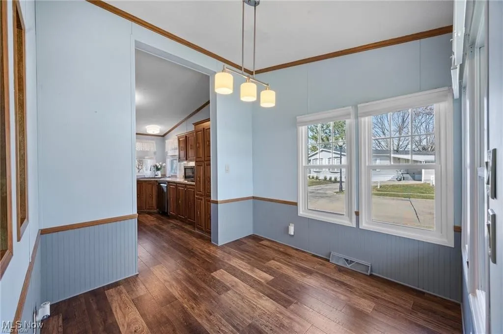 Unfurnished dining area with dark wood-type flooring, wainscoting, and vaulted ceiling