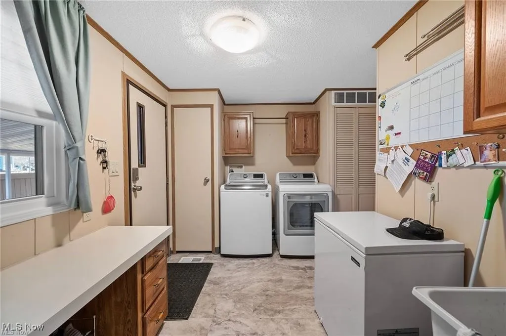 Laundry room with cabinet space, washer and clothes dryer, a textured ceiling, and ornamental molding