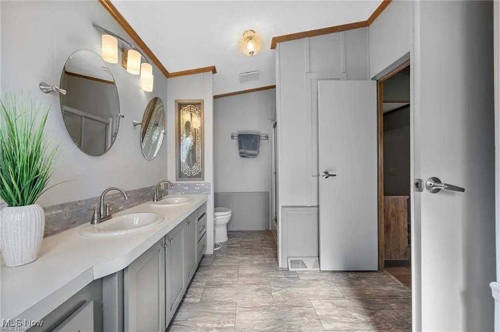 Bathroom featuring double vanity, ornamental molding, and a wainscoted wall