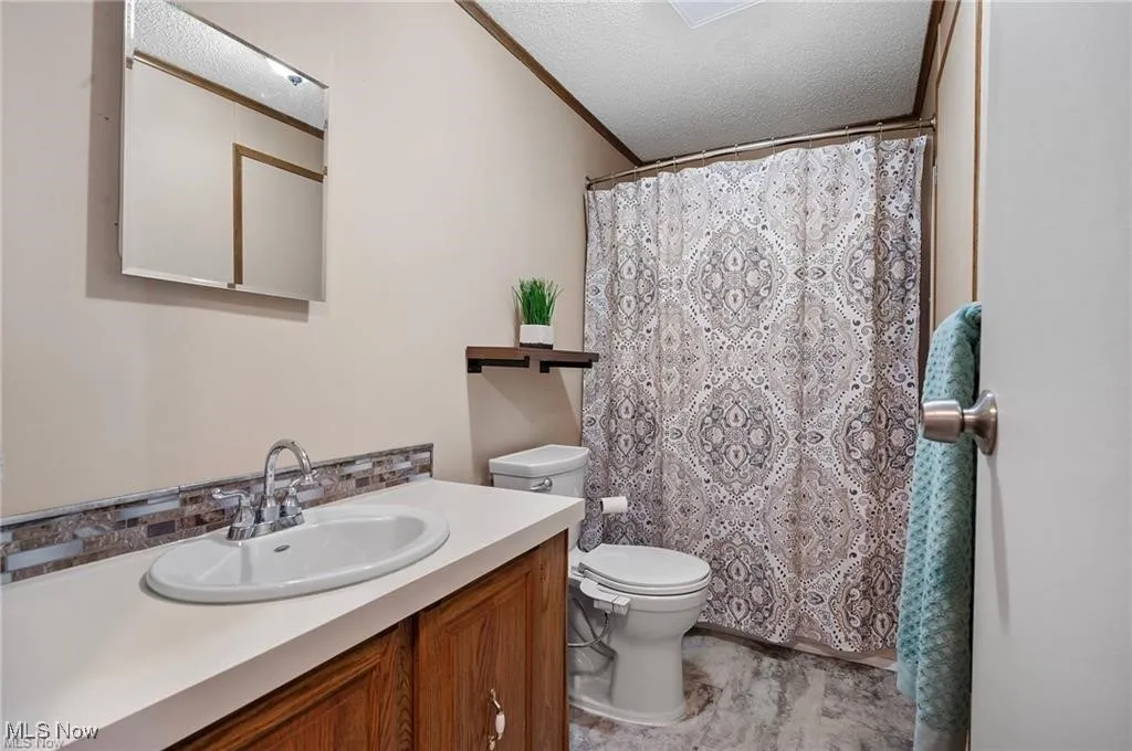 Bathroom with vanity, a textured ceiling, a shower with curtain, and tasteful backsplash