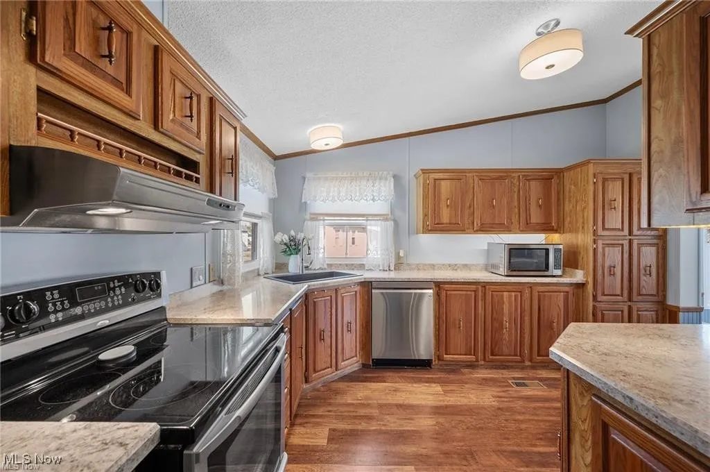 Kitchen with appliances with stainless steel finishes, lofted ceiling, ornamental molding, range hood, and brown cabinets