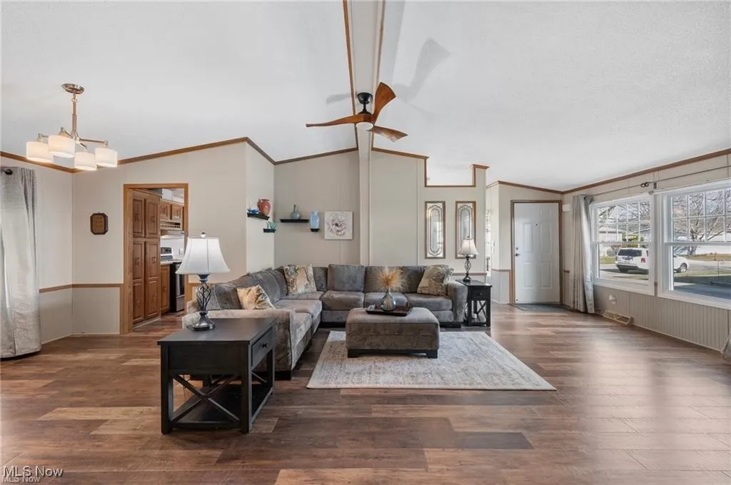 Living area with ceiling fan, ornamental molding, lofted ceiling, and wood finished floors