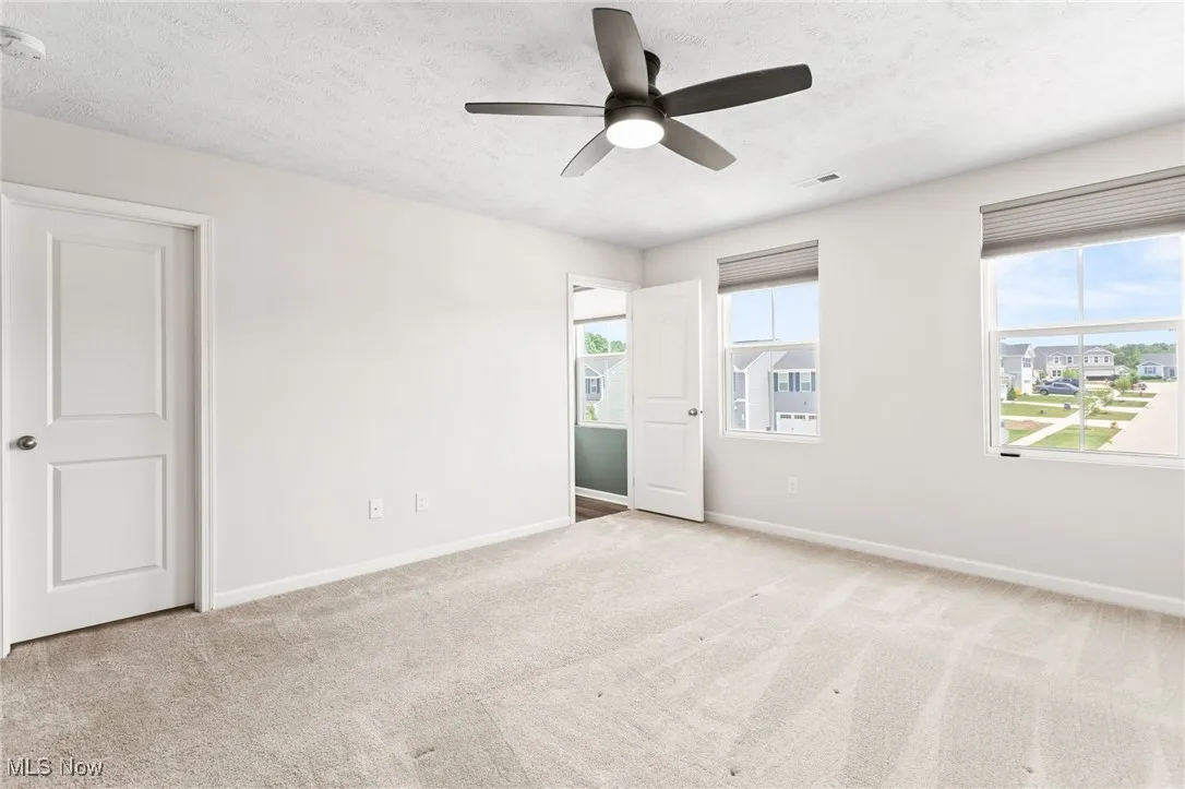 Unfurnished bedroom featuring a textured ceiling, multiple windows, carpet, and a ceiling fan