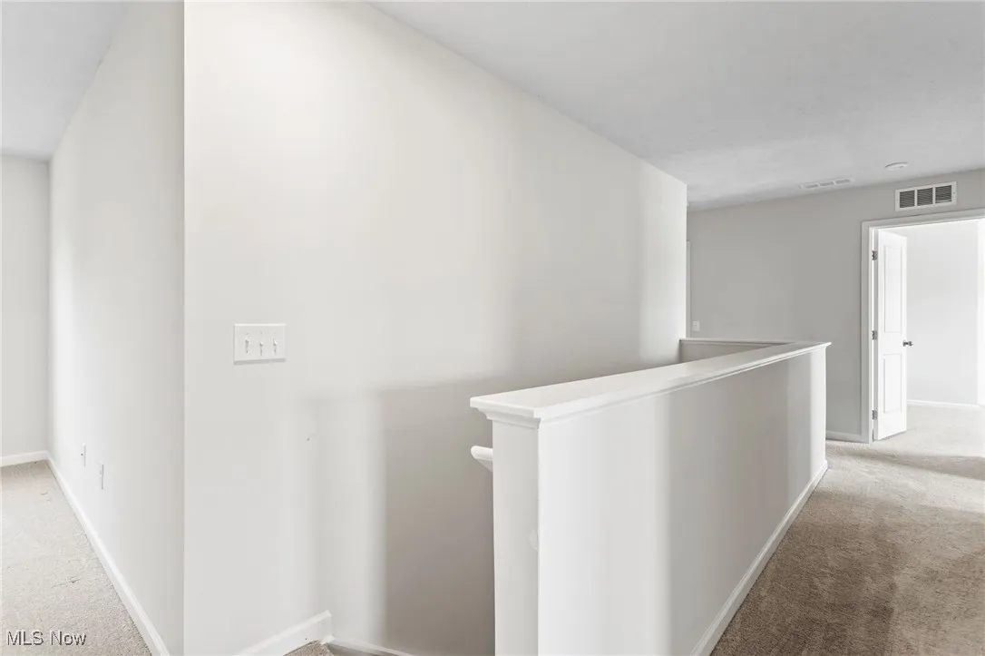 Hallway featuring an upstairs landing and light colored carpet