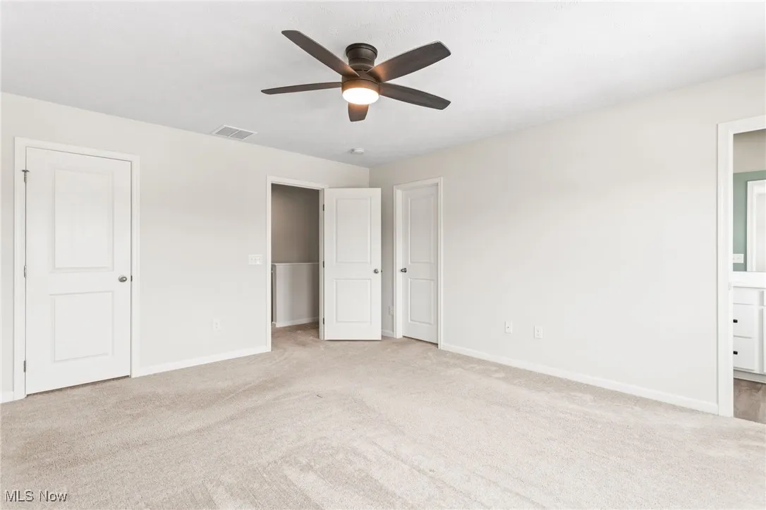 Unfurnished bedroom with light carpet, connected bathroom, and a ceiling fan