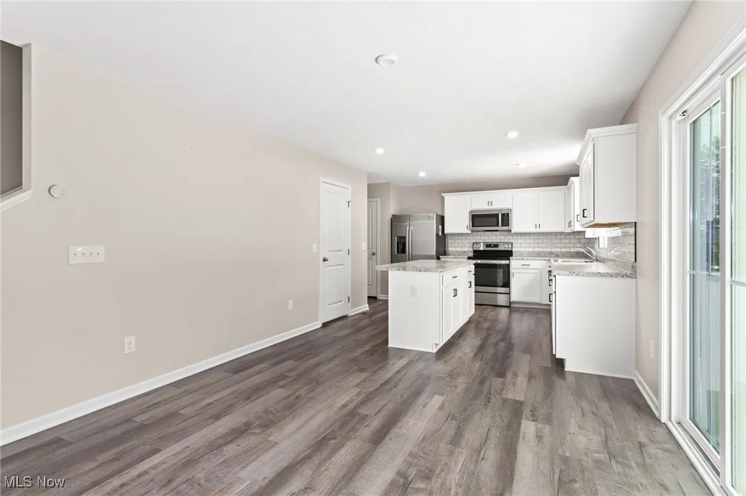 Kitchen with appliances with stainless steel finishes, a kitchen island, dark wood-type flooring, decorative backsplash, and white cabinetry