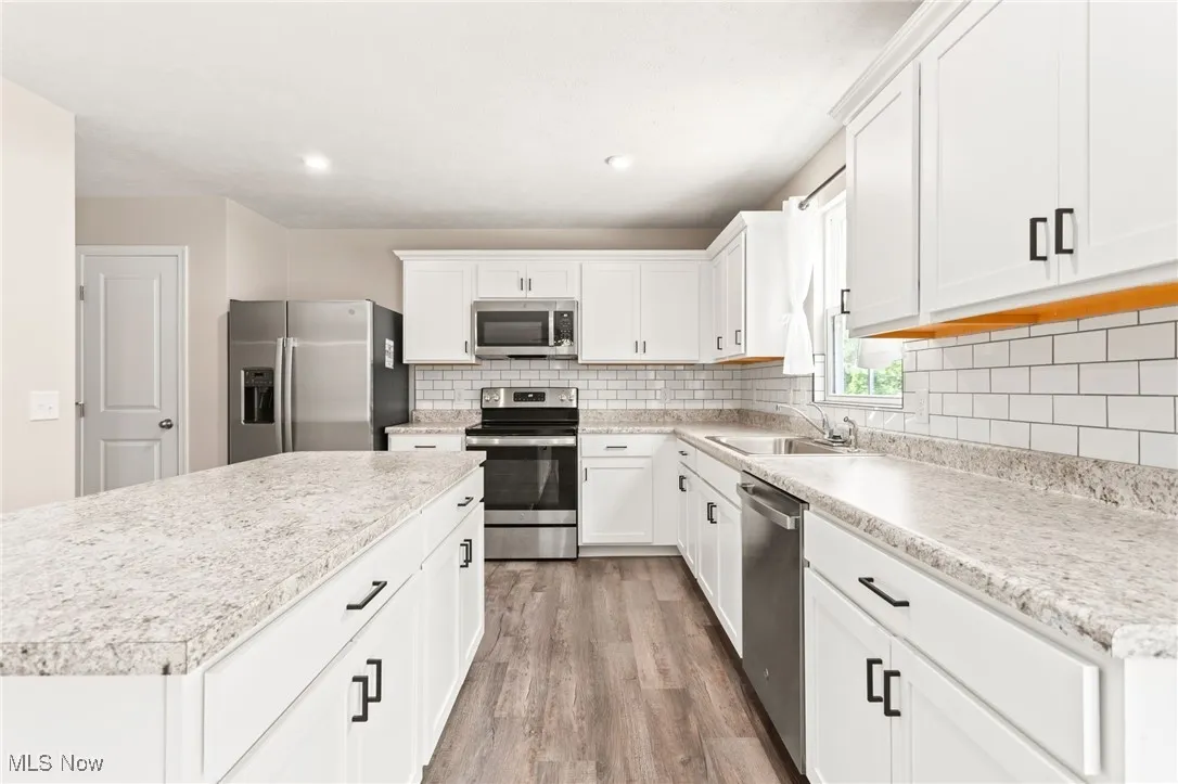 Kitchen with appliances with stainless steel finishes, light wood finished floors, backsplash, white cabinets, and recessed lighting