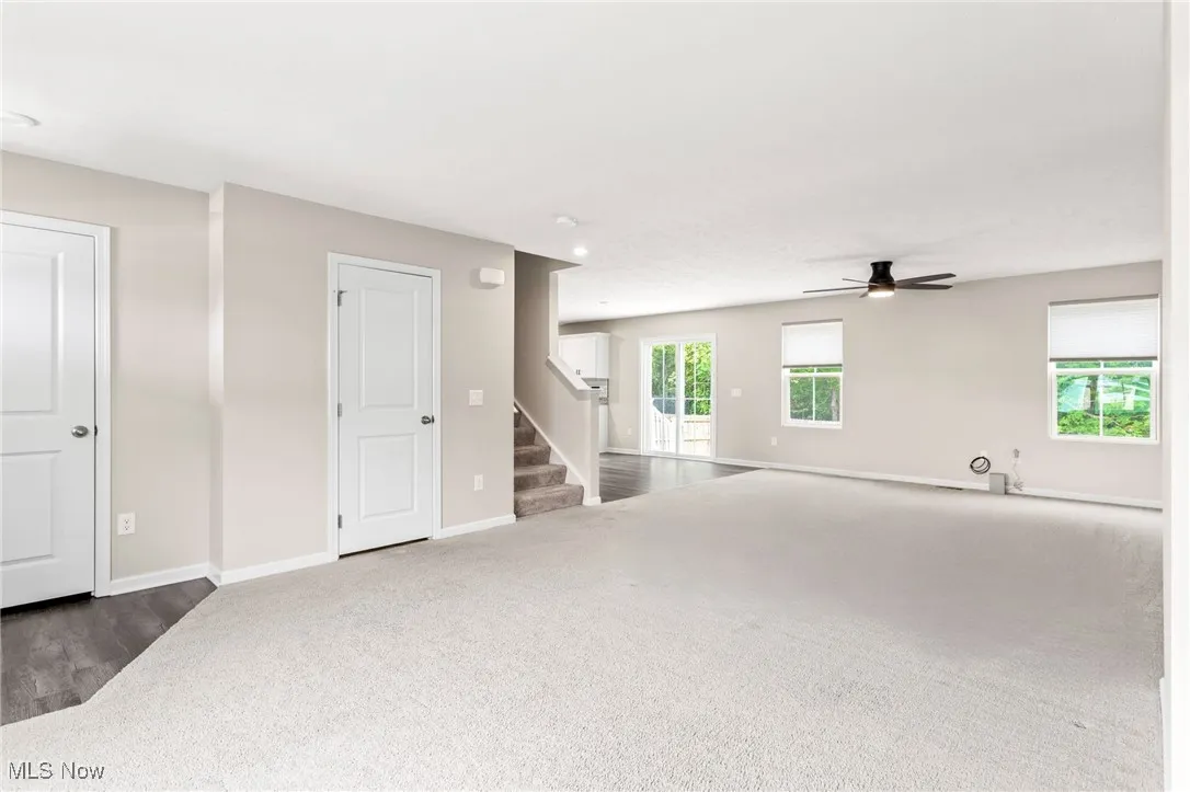 Unfurnished living room with dark colored carpet, a ceiling fan, and stairway