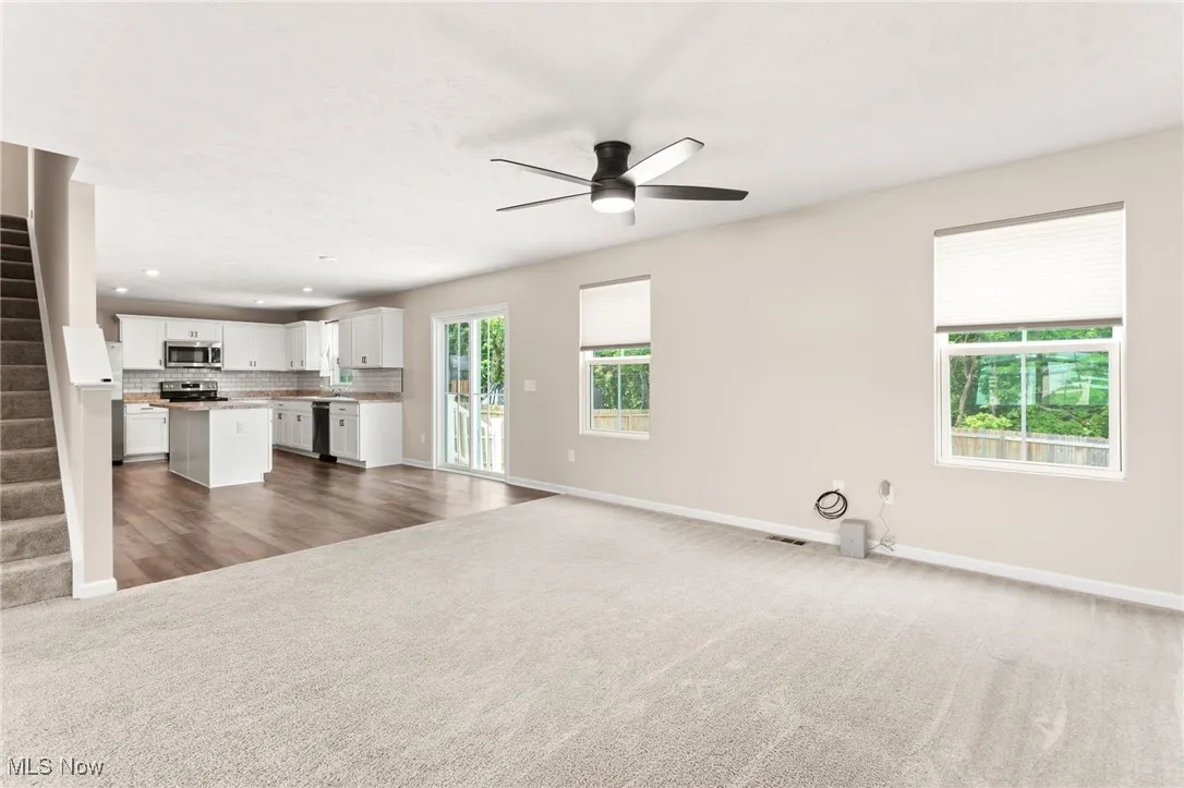 Unfurnished living room with carpet flooring, a ceiling fan, recessed lighting, and stairway