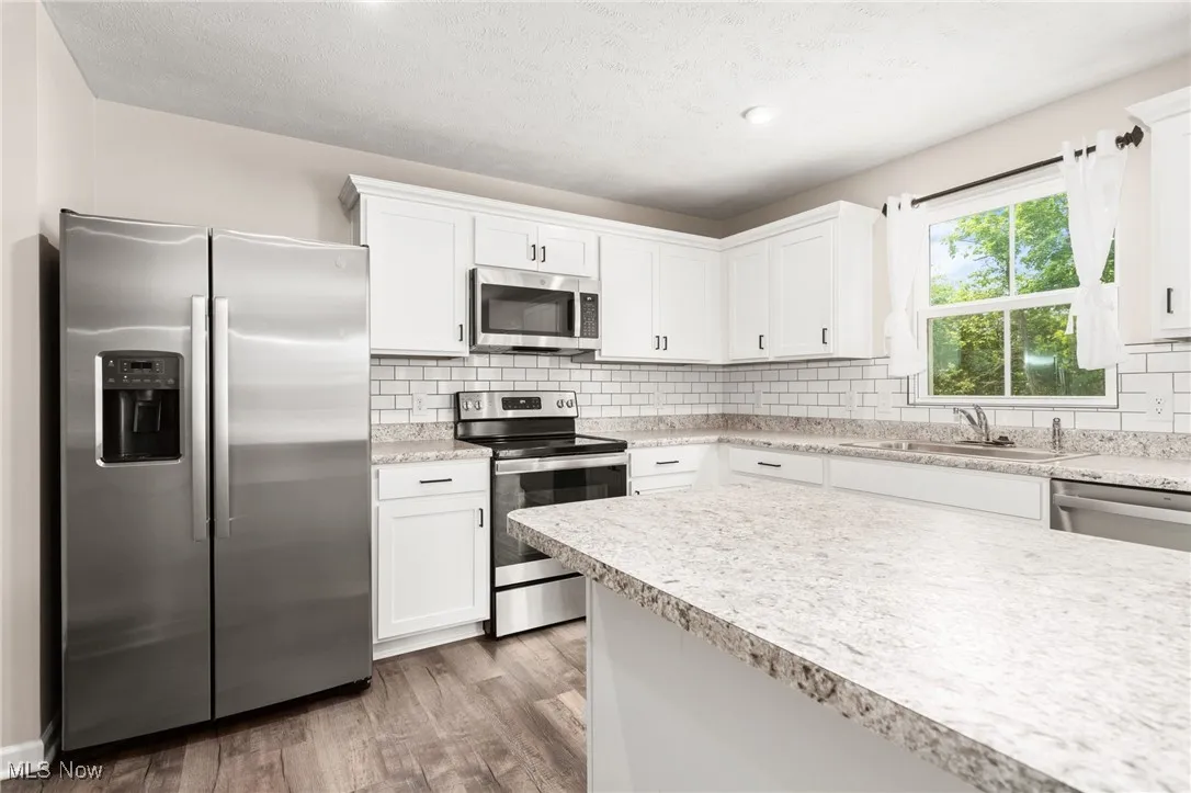 Kitchen featuring stainless steel appliances, light countertops, tasteful backsplash, wood finished floors, and white cabinetry
