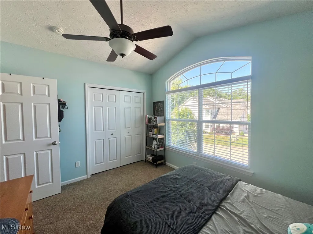Bedroom featuring lofted ceiling, carpet, a closet, a textured ceiling, and a ceiling fan