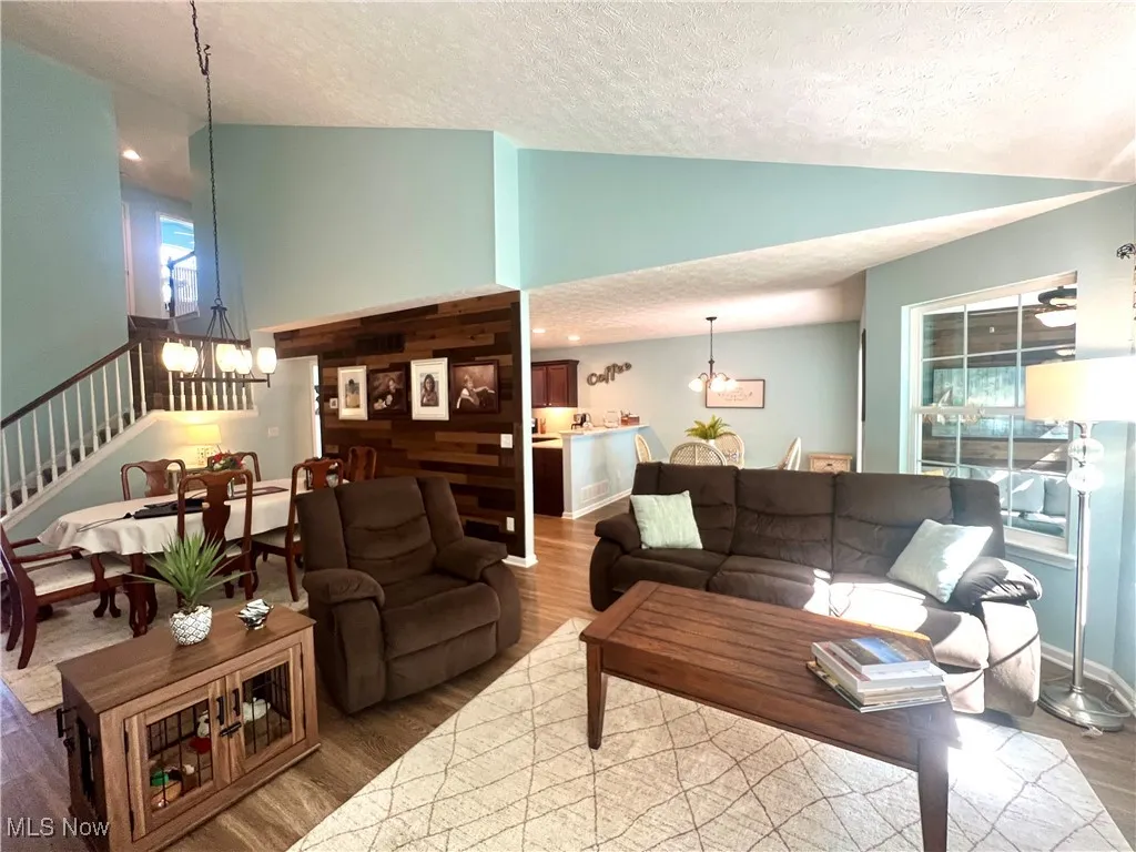 Living area with a chandelier, lofted ceiling, a textured ceiling, wood finished floors, and stairway