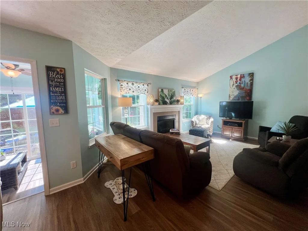 Living room with a fireplace, a textured ceiling, wood finished floors, and vaulted ceiling