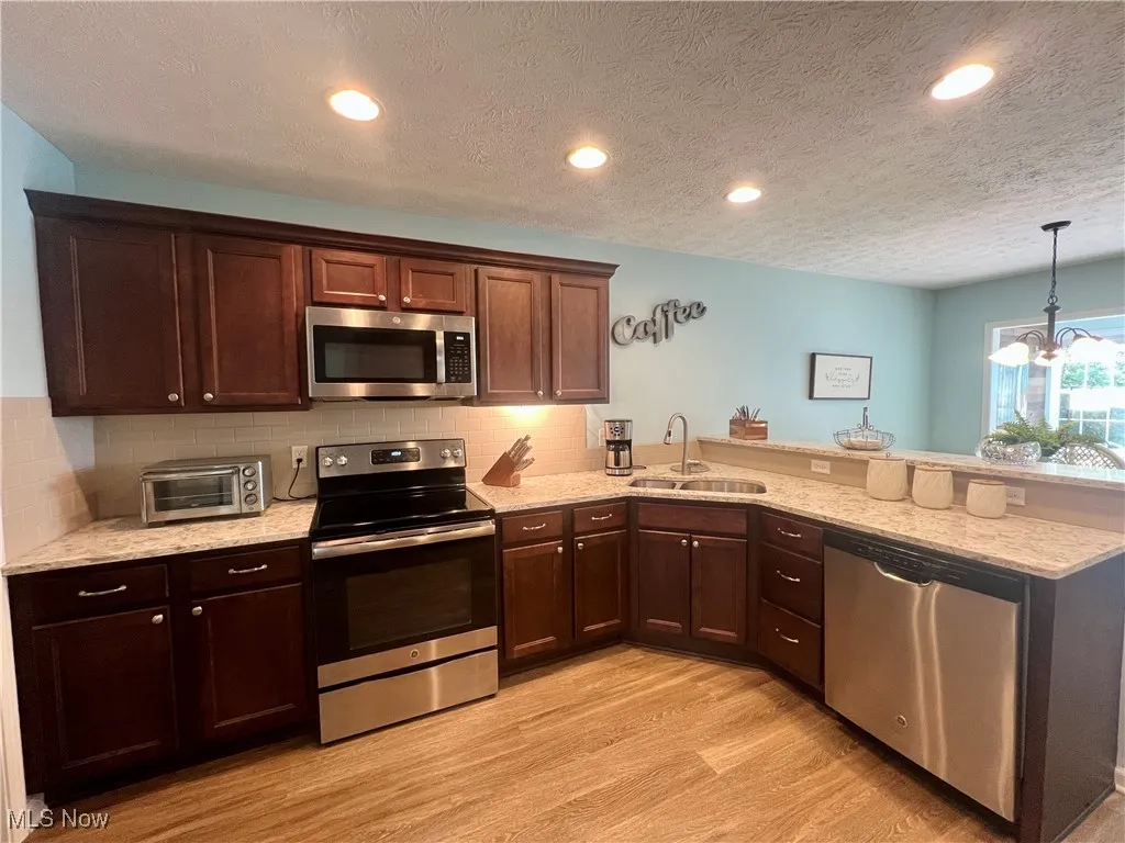 Kitchen featuring stainless steel appliances, a peninsula, light wood-style flooring, backsplash, and light counters
