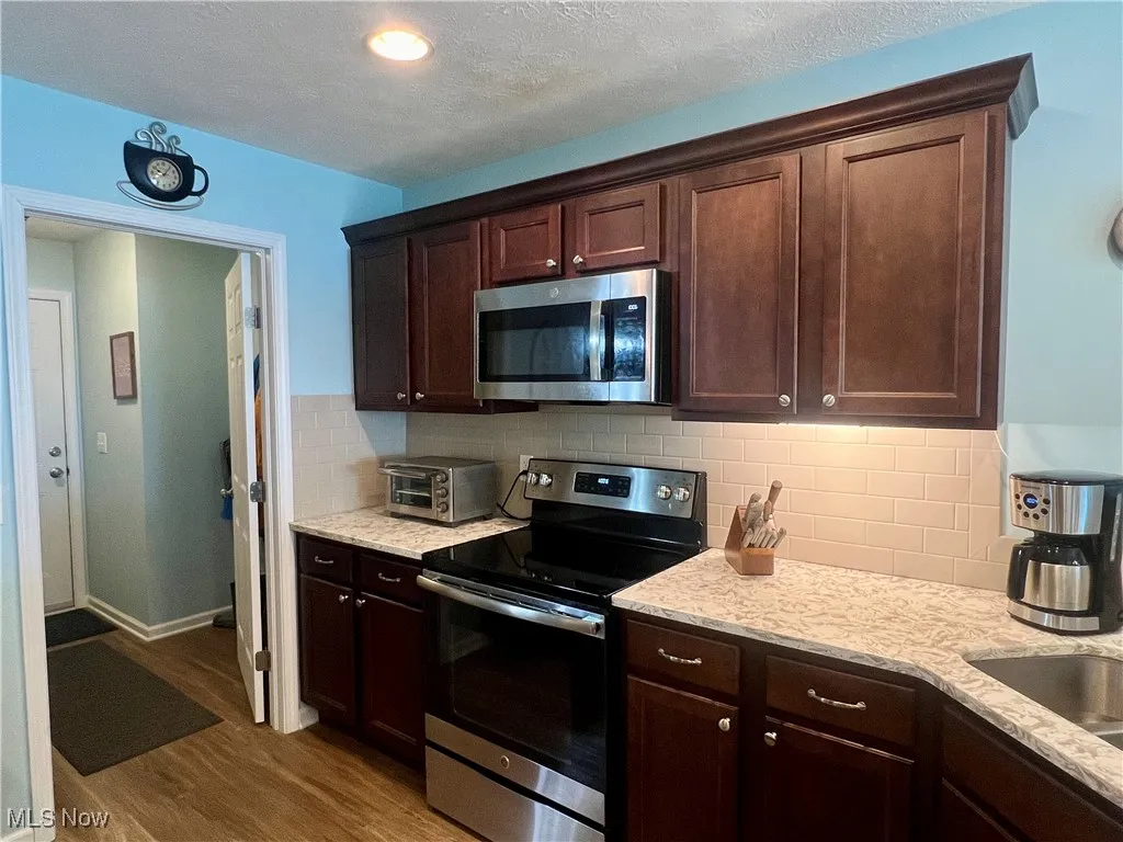 Kitchen featuring appliances with stainless steel finishes, wood finished floors, light stone counters, dark brown cabinetry