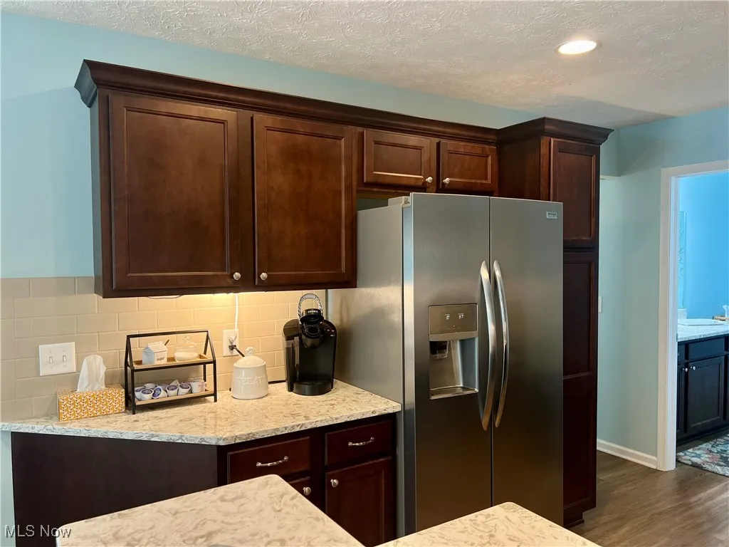 Kitchen with stainless steel fridge, dark wood finished floors, decorative backsplash, dark brown cabinetry, and light countertops