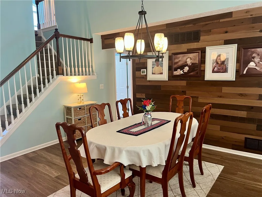 Dining room featuring a chandelier, wooden walls, wood finished floors, and stairs