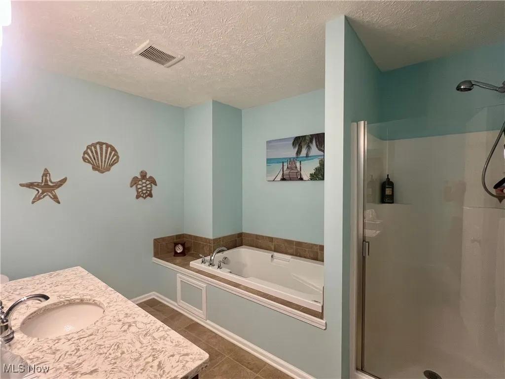 Bathroom featuring a shower stall, a garden tub, a textured ceiling, vanity, and tile patterned floors