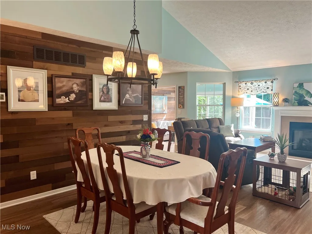 Dining room with wooden walls, a chandelier, a textured ceiling, wood finished floors, and high vaulted ceiling