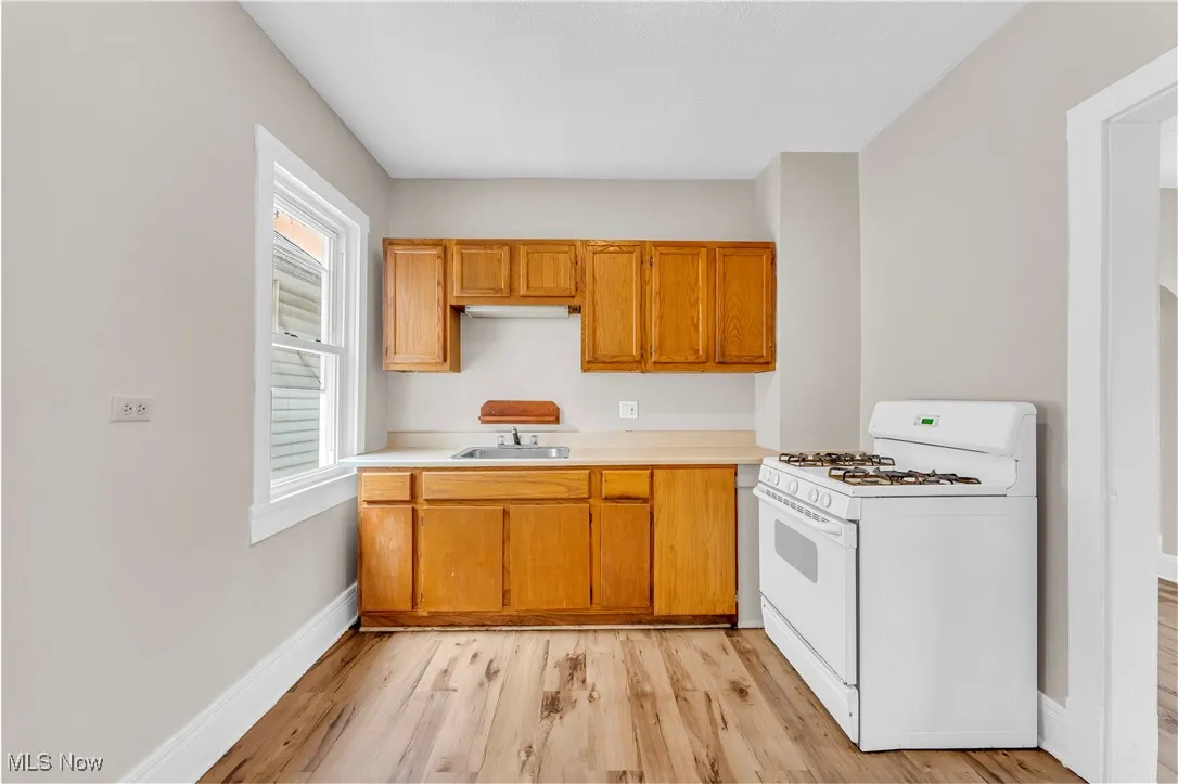 Kitchen featuring white gas stove, light countertops, light wood-type flooring, and brown cabinets