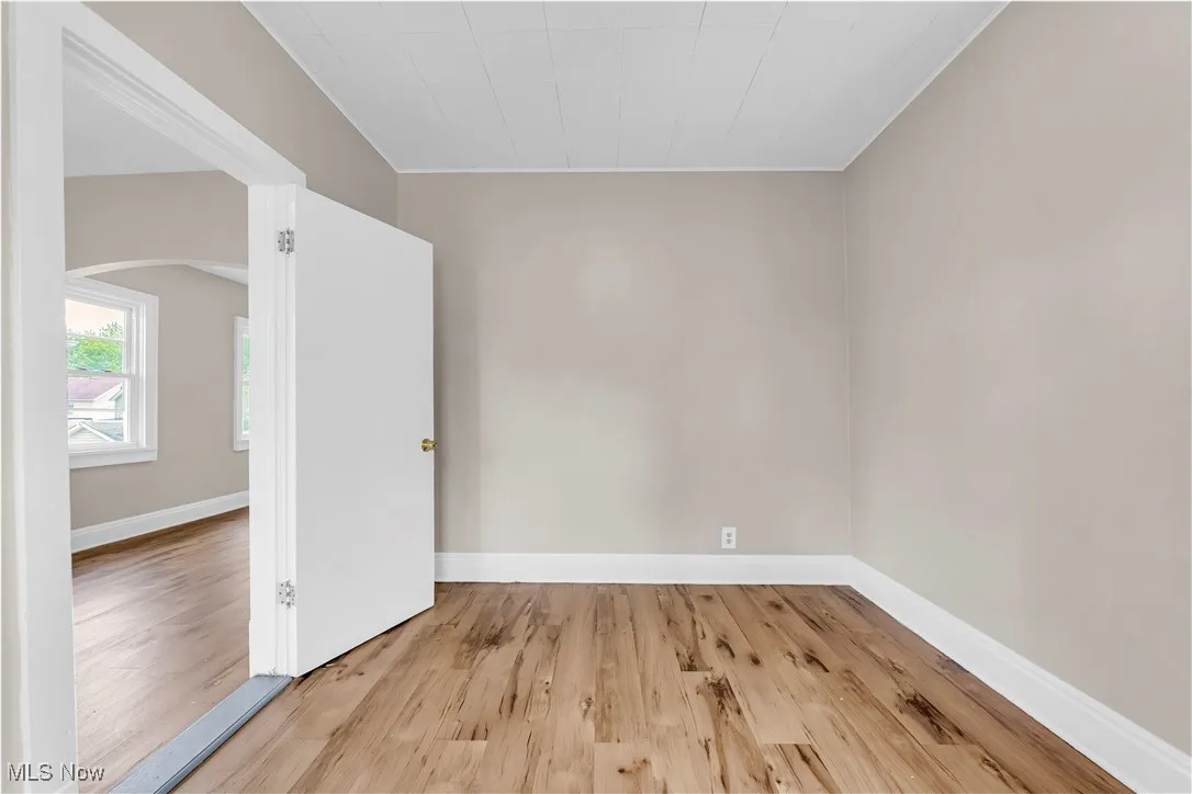 Spare room with arched walkways, wood finished floors, and crown molding