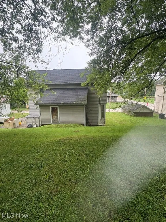 View of side of property with a shingled roof and a yard