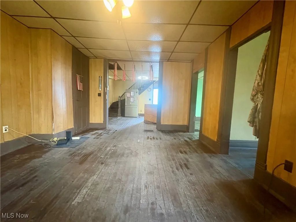 Unfurnished room with hardwood / wood-style floors, a drop ceiling, stairway, wood walls, and heating unit