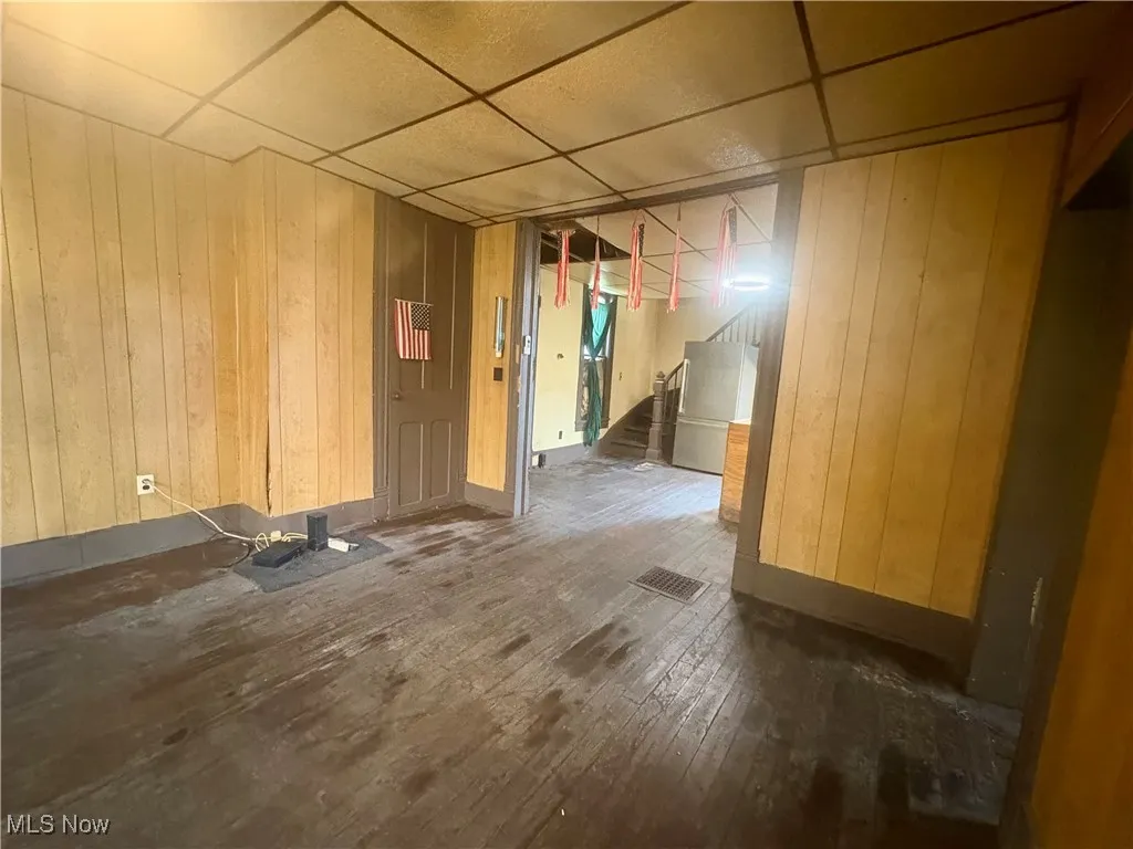 Empty room with a drop ceiling, wood-type flooring, wooden walls, and stairs