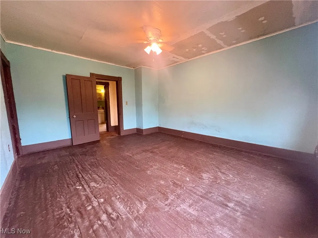 Spare room featuring dark wood-style floors, a ceiling fan, and crown molding