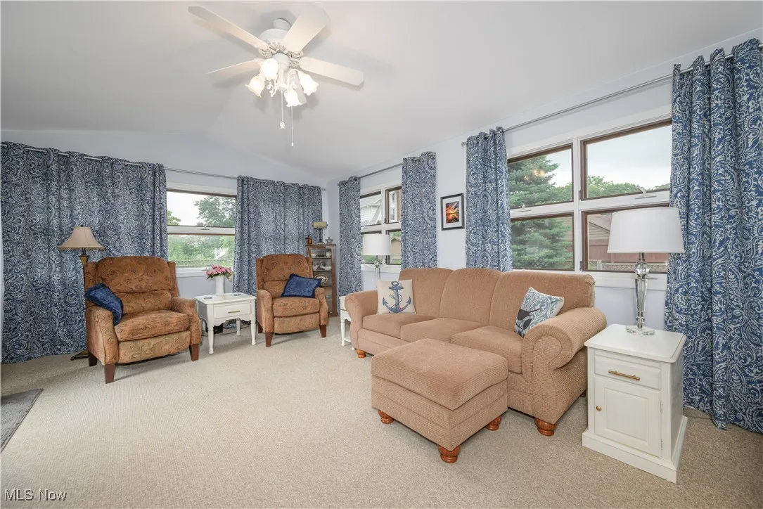 Family room/sunroom addition with light colored carpet, vaulted ceiling, and a ceiling fan overlooks the backyard with outdoor access.