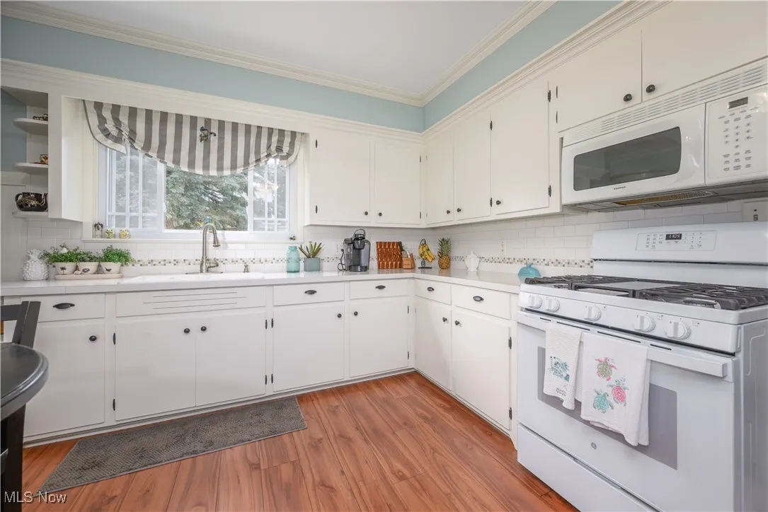 Kitchen featuring white appliances, light countertops, crown molding, tasteful backsplash, and LVT flooring.