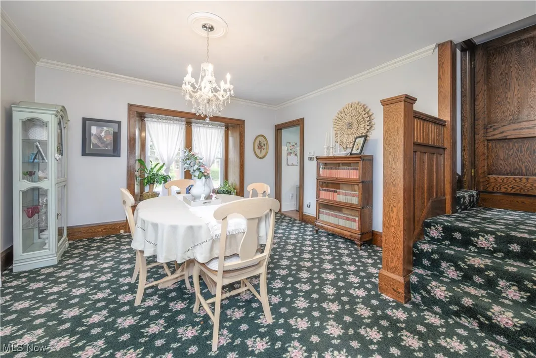 Dining room featuring crown molding, a built- in window seat and crystal chandelier.  Staircase to upper levels and doorway leading to the kitchen.
