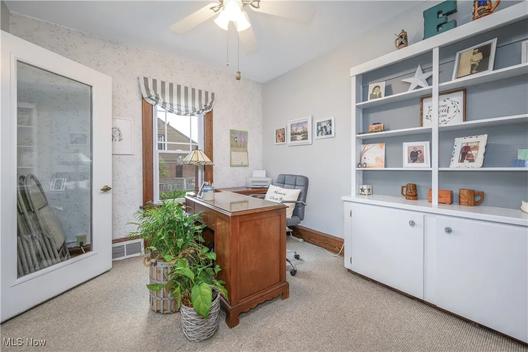 Home office featuring built-in bookcase and storage, a ceiling fan, and light carpet.