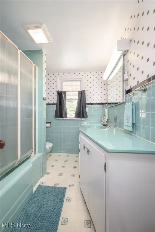 Bathroom featuring vanity, combined bath / shower with glass door, tile walls, and vinyl flooring.