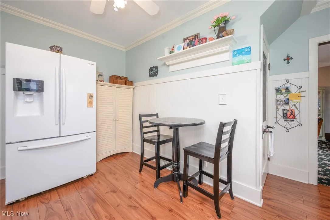 Kitchen with white fridge , ornamental molding, wainscoting, and ceiling fan. Door leads to the basement