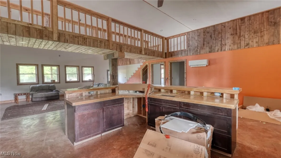 Kitchen featuring finished concrete floors, a wall mounted air conditioner, open floor plan, a kitchen island, and a high ceiling