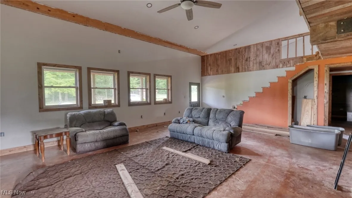 Living area with high vaulted ceiling, ceiling fan, and stairs